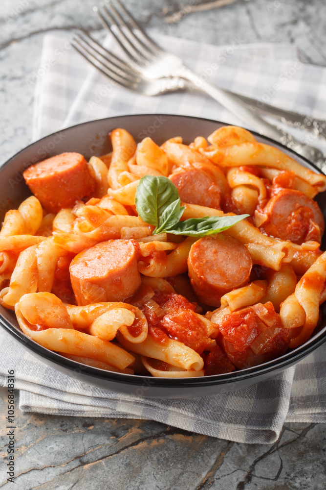 Italian Treccione pasta served with tomato, onion, sausage and basil close-up in a bowl on the table. Vertical Italian Treccione pasta served with tomato, onion, sausage and basil close-up in a bowl on the table. Vertical