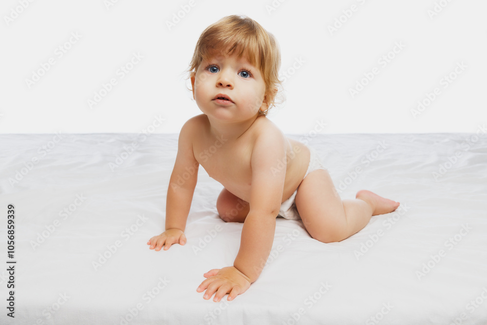 Growth and development. Baby kneeling with both hands on bed, looking inquisitively upward against white studio background. Concept of parenthood, natural beauty, love and care. Ad. Growth and development. Baby kneeling with both hands on bed, looking inquisitively upward against white studio background. Concept of parenthood, natural beauty, love and care. Ad.