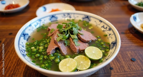 A bowl of pho with sliced beef, fresh herbs, and lime wedges