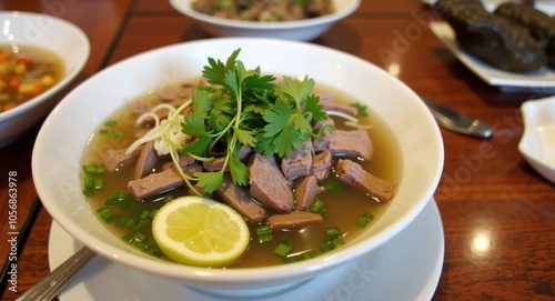 A bowl of pho with sliced beef, fresh herbs, and lime wedges