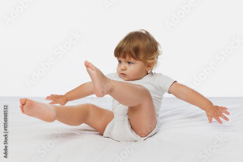 Little, funny baby-boy playfully balancing with legs up, dressed in white onesie against white studio background. Concept of parenthood, natural beauty, love and care. Ad.