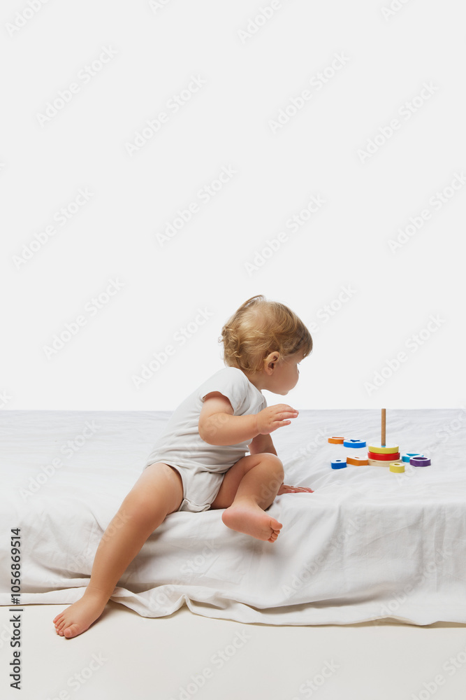 Little baby in white onesie, reaching towards colorful toys on white bed, showcasing curiosity and motor skill development. Concept of parenthood, natural beauty, love and care. Ad. Little baby in white onesie, reaching towards colorful toys on white bed, showcasing curiosity and motor skill development. Concept of parenthood, natural beauty, love and care. Ad.
