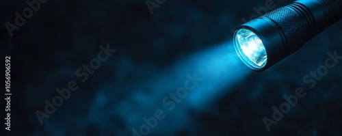 A handheld flashlight emits a bright blue beam in the dark, creating a focused light source with dramatic contrast against the background.