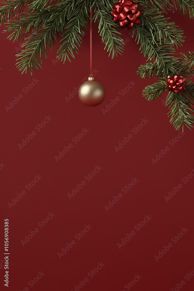 Gold bauble hangs from fir branch against red background