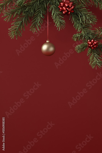 Gold bauble hangs from fir branch against red background