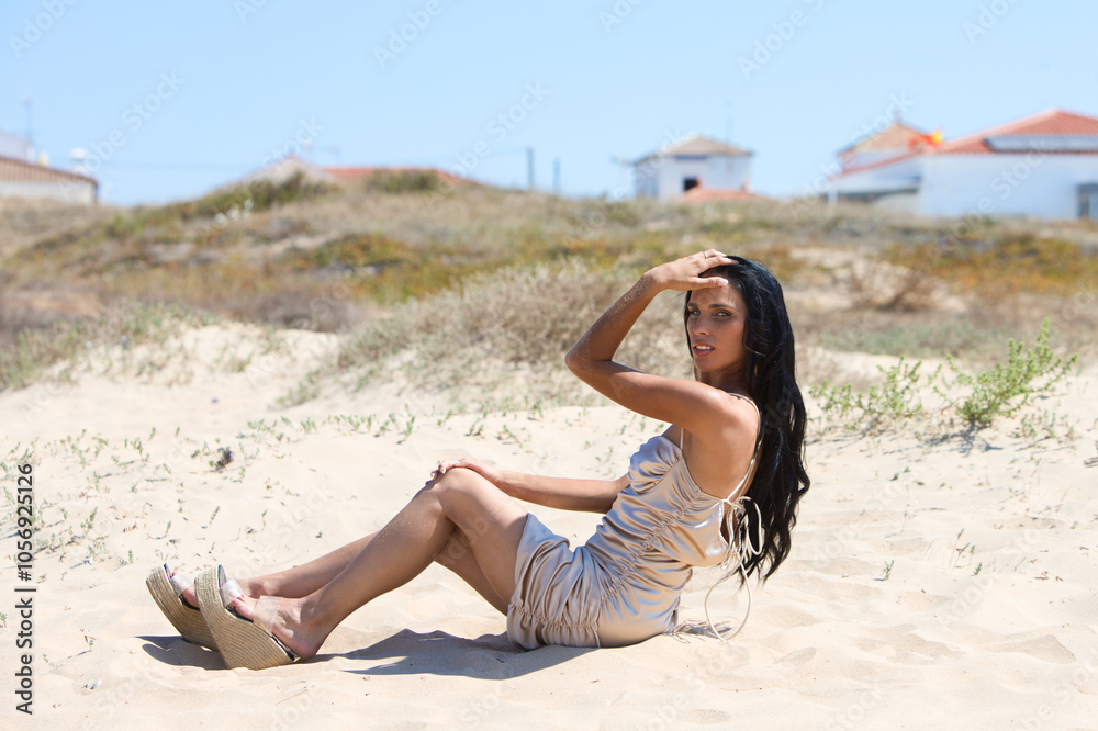 beautiful young brunette woman with long hair lying on a fine golden sand dune on a beach in the south of Spain in andalusia. The woman is wearing make-up, a long golden dress and high heels. beautiful young brunette woman with long hair lying on a fine golden sand dune on a beach in the south of Spain in andalusia. The woman is wearing make-up, a long golden dress and high heels.