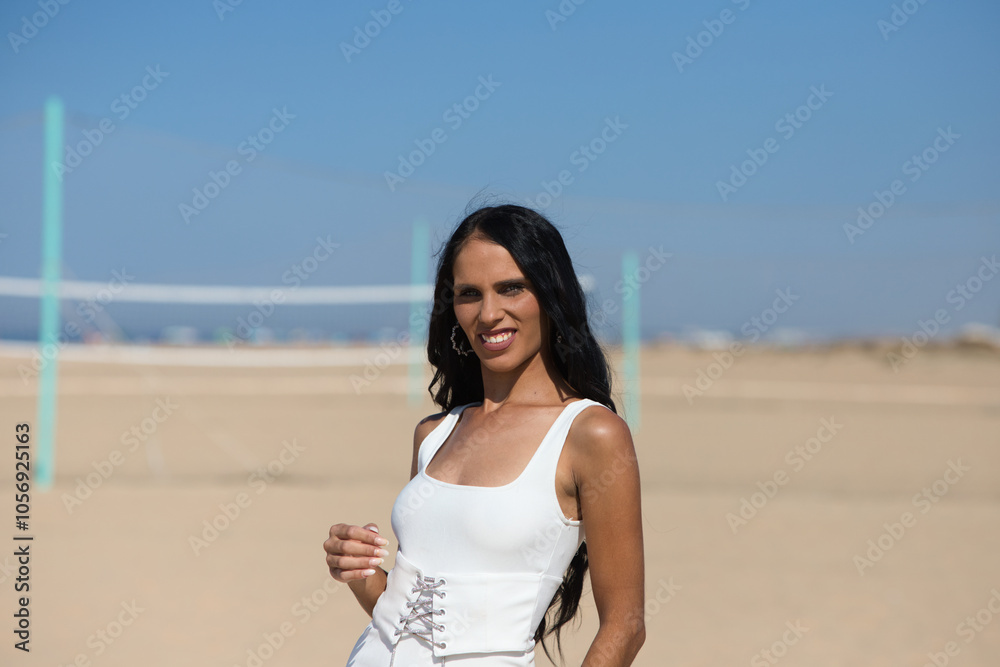 A beautiful young woman with long hair and an elegant white dress walks along the wooden walkway on the sandy beach. In the background the blue sea and the umbrellas of the holidaymakers. A beautiful young woman with long hair and an elegant white dress walks along the wooden walkway on the sandy beach. In the background the blue sea and the umbrellas of the holidaymakers.
