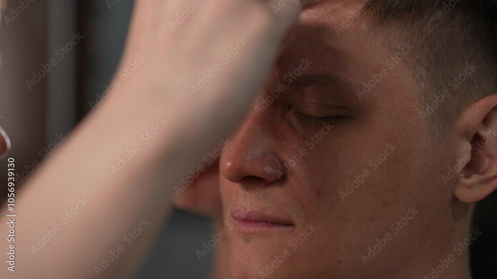 Closeup of female beautician carefully shaping eyebrows of young man with closed eyes, using tweezers to remove stray hairs and define their shape. Concept of modern male lifestyle and body care. Closeup of female beautician carefully shaping eyebrows of young man with closed eyes, using tweezers to remove stray hairs and define their shape. Concept of modern male lifestyle and body care.