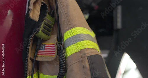 Fireman jacket known as bunker or turnout safety gear hanging on firetruck door ready to be used in case of emergency. Special equipment for firefighters in station. USA flag embedded on jacket
