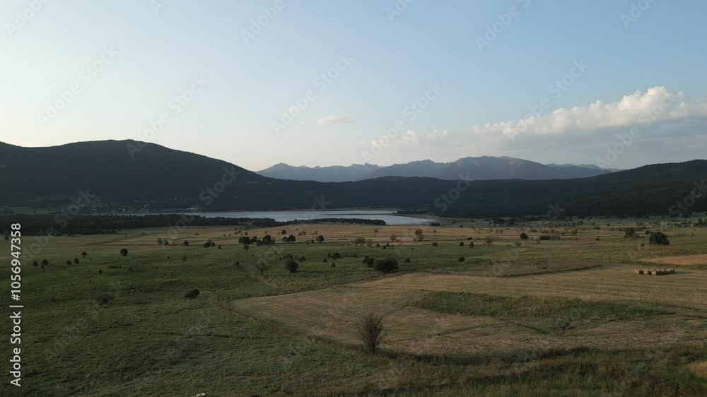Camera movement pans left, showcasing a stunning mountain lake nestled within a lush green meadow. The scene captures the tranquil beauty of nature under a clear blue sky Camera movement pans left, showcasing a stunning mountain lake nestled within a lush green meadow. The scene captures the tranquil beauty of nature under a clear blue sky
