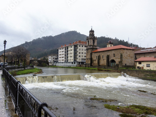 Horizontal panoramic view of the touristic village Balmaseda in the Basque country with a large river surrounded by houses and small waterfalls and in the background its medieval stone bridge.