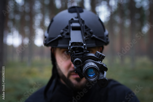 A man with a beard in a tactical helmet with a night vision device in a dark forest. Soft focus photo.