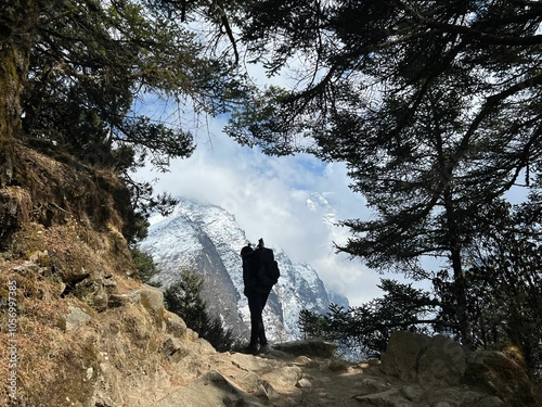 Person silhouette standing on a trail against snowcapped mountains under a clear sky