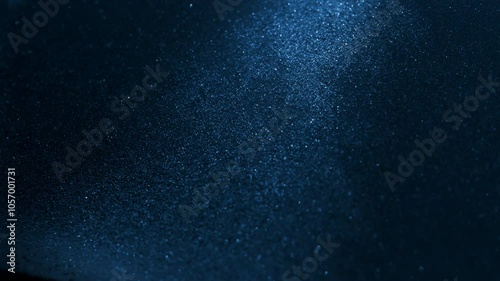 Little grains of sand falling in abstract slow motion under blue light. 