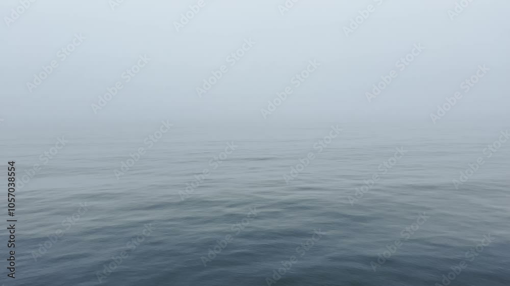 Calm ocean waves ripple gently under a thick layer of fog, obscuring the horizon and blending sea and sky into a seamless, muted gray expanse, evoking a sense of tranquility and mystery Calm ocean waves ripple gently under a thick layer of fog, obscuring the horizon and blending sea and sky into a seamless, muted gray expanse, evoking a sense of tranquility and mystery