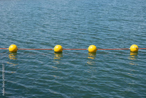 Billede på lærred a line of bright yellow buoys floating on calm blue sea water, connected by an orange rope