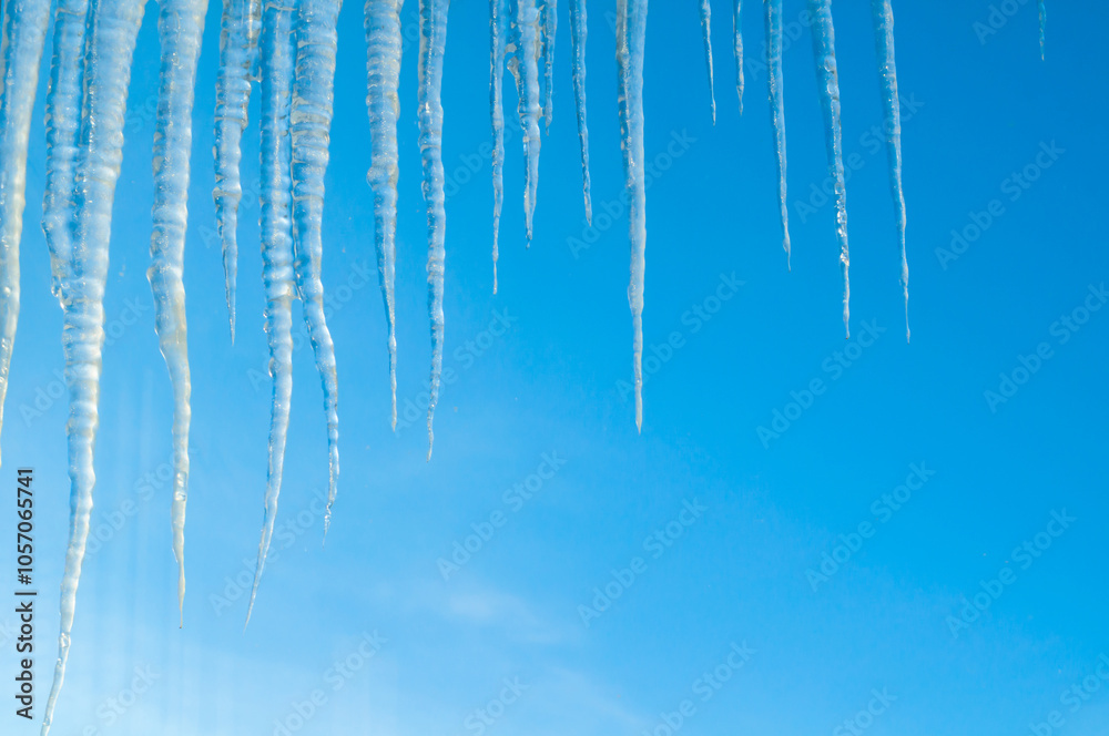 Winter background, long frozen icicles on the roof on the background of the blue sky, natural long icicles, winter background Winter background, long frozen icicles on the roof on the background of the blue sky, natural long icicles, winter background