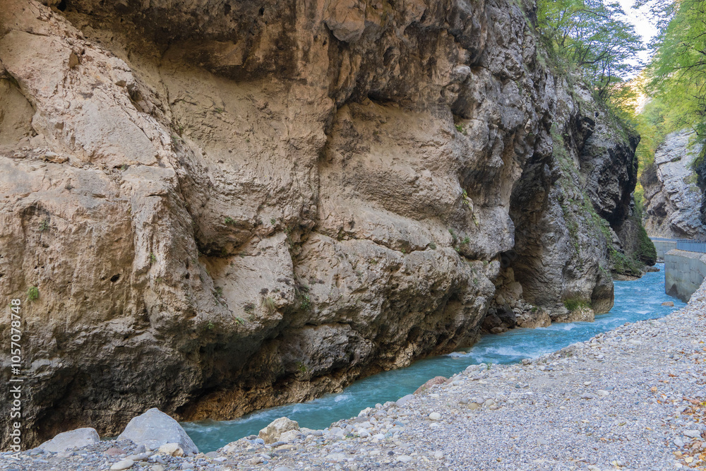 Obraz premium Steep cliffs hang over mountain river with emerald-clear water. Stormy Chegem River flows in deep crevice along bottom of Chegem Gorge. In depths of gorge, semi-darkness reigns.