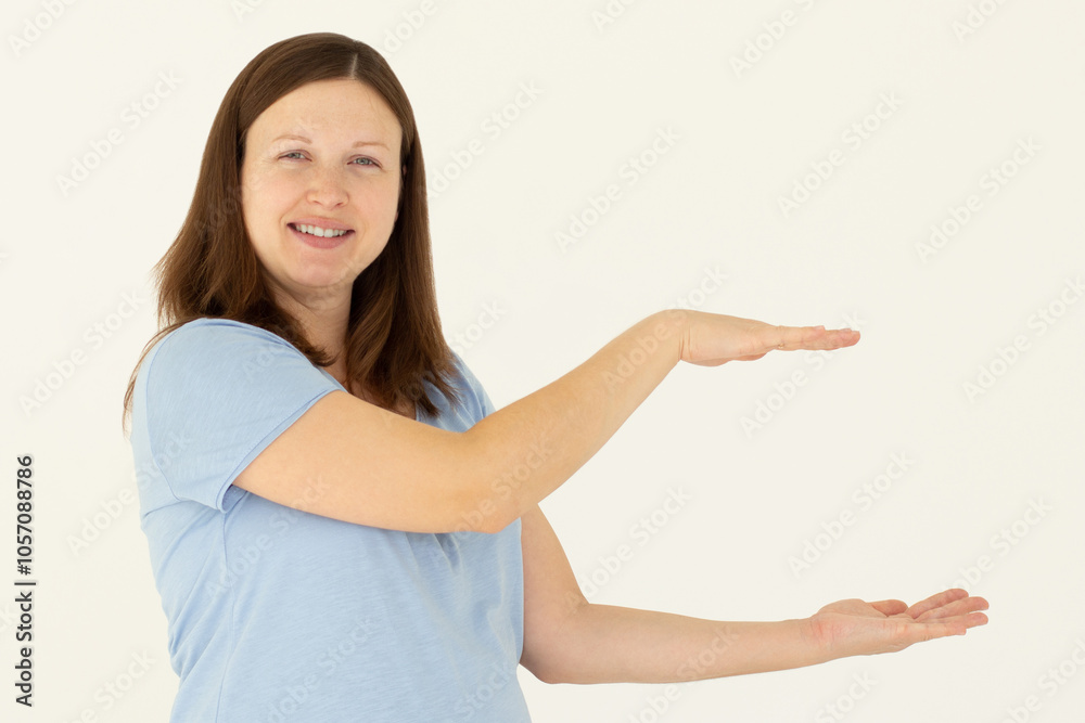 Young confident woman showing logo on empty space between arms. Smiling girl inviting or advertising promo deal, pointing hands right and looking at camera, white background. Young confident woman showing logo on empty space between arms. Smiling girl inviting or advertising promo deal, pointing hands right and looking at camera, white background.