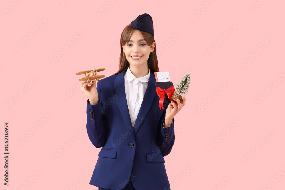 Young stewardess with passport, wooden airplane and Christmas tree on pink background Young stewardess with passport, wooden airplane and Christmas tree on pink background