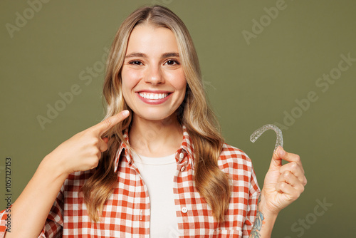 Young smiling woman she wear red shirt white t-shirt casual clothes hold in hand transparent aligners point finger on teeth isolated on plain pastel green background studio portrait Lifestyle concept photo