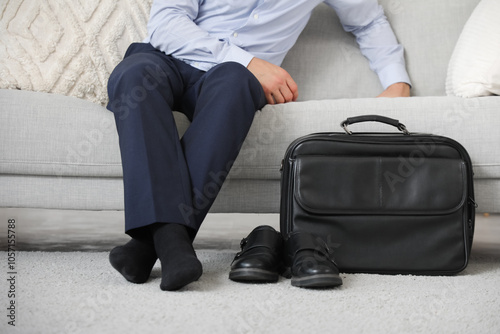 Young businessman with removed shoes and briefcase resting on his day off at home