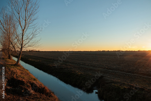 Obraz na płótnie sole che tramonta sulla linea dell'orizzonte e colora di arancione il cielo azzurro e sereno, con vista panoramica da un ambiente di campagna in autunno w salonie