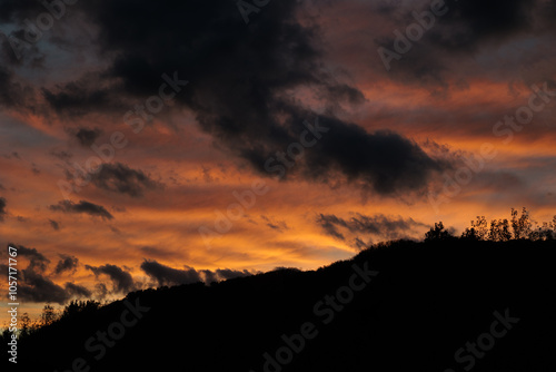 Obraz na płótnie sole che tramonta dietro ad una collina e colora il cielo e le nuvole di arancione w salonie
