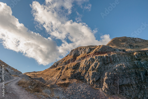 vista panoramica che guarda verso i pendii rocciosi ed erbosi della cima di un monte nel nord Italia, sotto un cielo azzurro, coperto da qualche nuvola leggera e bianca, di giorno, in autunno photo