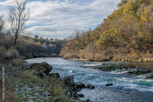 vista panoramica frontale, a livello del terreno, del fiume Isonzo, in Slovenia, circondato da boschi lungo le ripide sponde, in autunno, sotto un cielo nuvoloso photo