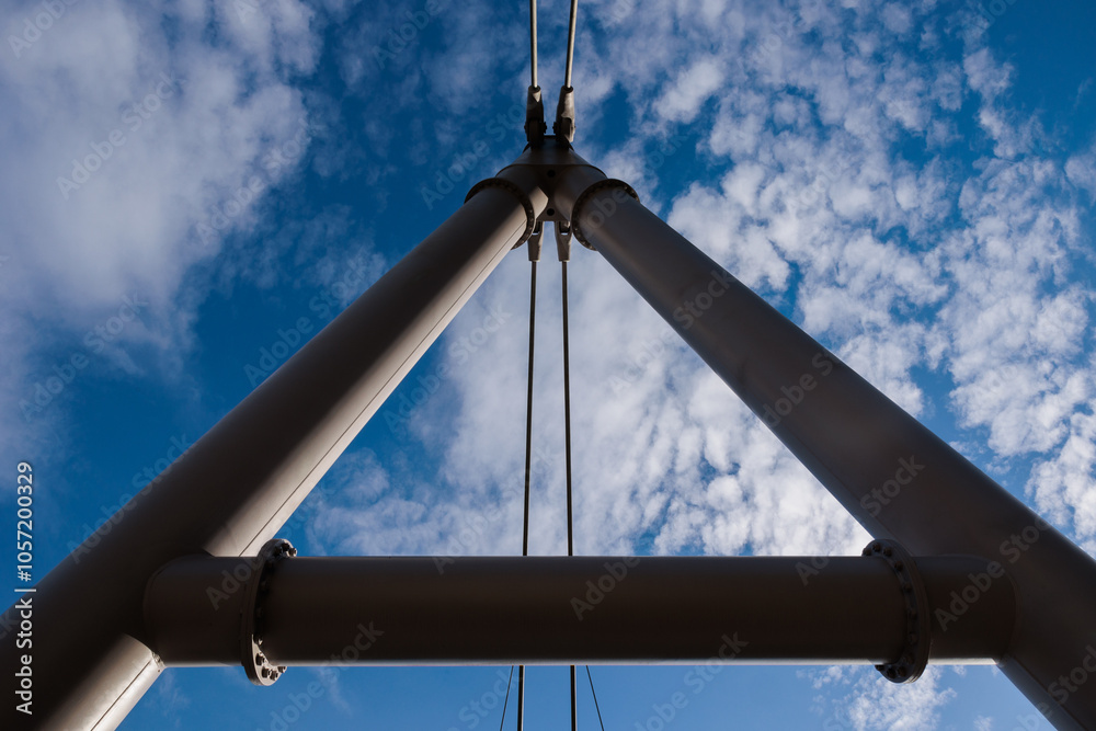 stralli o pilastri di un ponte che si uniscono in una forma triangolare, visti dal basso, guardando verso il cielo azzurro, con alcune nuvole bianche