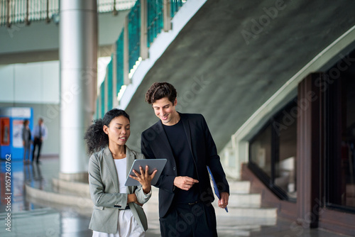 Businessman in black suit walking and discussing with businesswoman in casual suit with tablet before meeting with partner at party club.