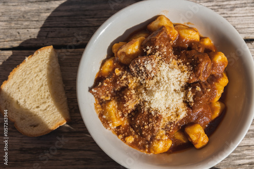 piatto di gnocchi col ragù di carne ed una piccola fetta di pane fresco, su un tavolo di legno, di giorno, a pranzo, visto da sopra photo