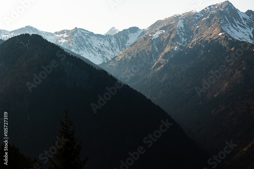 dettaglio su alcune cime e catene montuose innevate in alta quota, nelle Alpi Italiane, di pomeriggio, con una leggera foschia, illuminate dal sole, in controluce photo