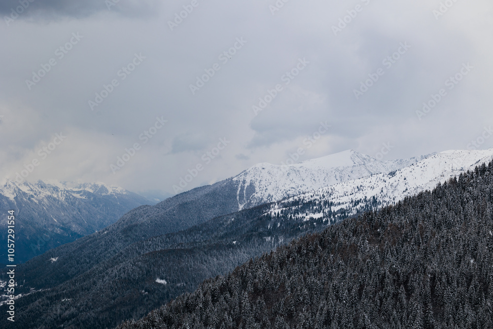 vista dettagliata di varie catene montuose lontane, completamente innevate, in un ambiente freddo e naturale di montagna nelle Alpi Italiane a nord est, sotto un cielo nuvoloso, in inverno
