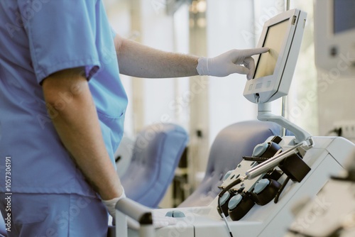 Medical professional in scrubs adjusting touchscreen on medical device in clinical setting while interacting with equipment. Focus on hand and device while working