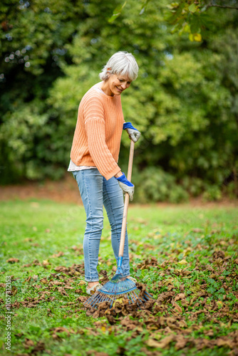 Obraz na plátně Senior woman raking leaves in an autumn garden