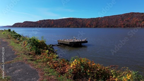 A low, aerial view of the Hudson River under the Mid-Hudson Bridge. Taken on a sunny day during the autumn season. The camera dolly in and pan right towards seagulls on a concrete slab, they fly away. photo