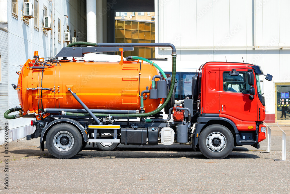 Modern orange and red sewage truck parked near industrial building.
