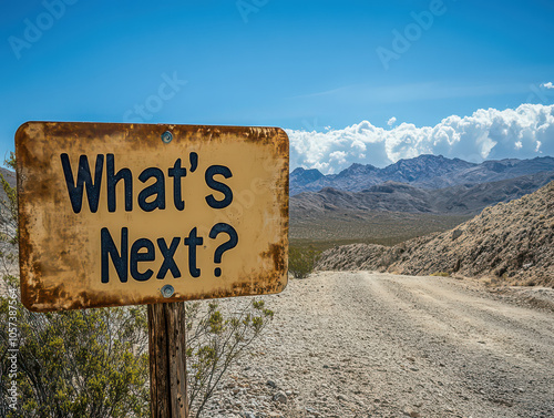 A rustic sign with 'What's Next?' along a remote desert road, with a dramatic mountain backdrop and clear blue sky.