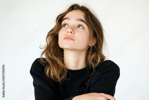 Thoughtful teen girl with arms crossed, looking up with pensive expression. Her wavy hair frames her face, creating serene atmosphere