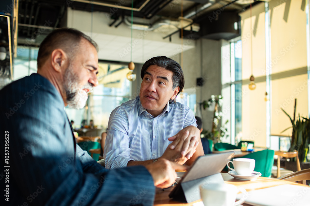 Businessmen discussing strategy over coffee in modern cafe setting Businessmen discussing strategy over coffee in modern cafe setting