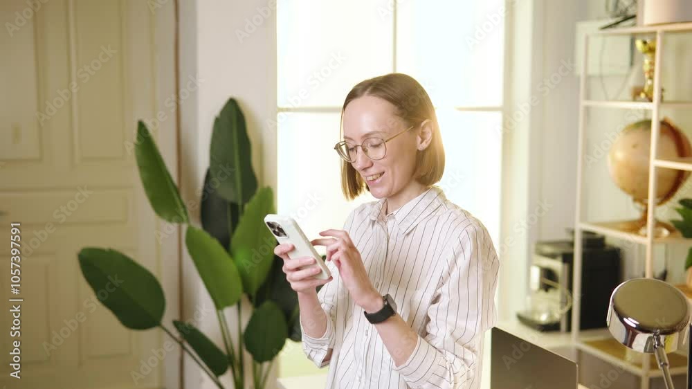 Woman smiling while using smartphone in a bright and airy living space with indoor plants Woman smiling while using smartphone in a bright and airy living space with indoor plants