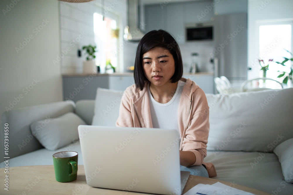 Asian woman working on laptop from home couch Asian woman working on laptop from home couch