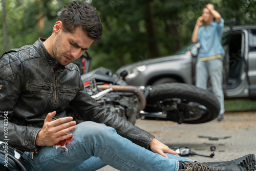 Motorcyclist sits on the asphalt near motorcycle, after road accidents with car. Broken and wrecked motorcycle on road