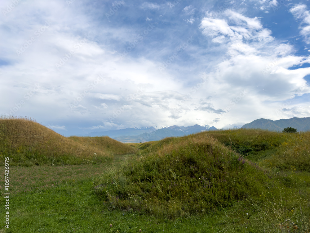 Green hilly landscape with scenic mountains in the background under a clear blue sky in the foothills of Kyrgyzstan. Green hilly landscape with scenic mountains in the background under a clear blue sky in the foothills of Kyrgyzstan.