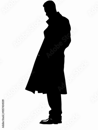 Man in a black coat stands in front of a white background. The man is wearing a trench coat and he is looking down