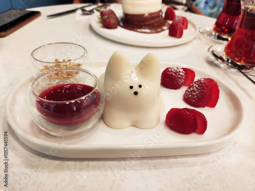 Delicious sweet white Japanese dessert, pudding in the shape of a cat, on a plate with strawberries and fruit sauce