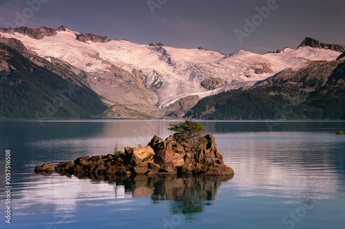 Tranquil lake and mountains with snow, and a small landform in the middle of the lake photo