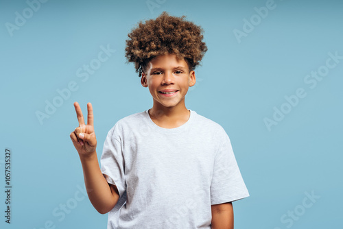 Happy attractive African American boy with curly hair wearing white t shirt showing peace sign